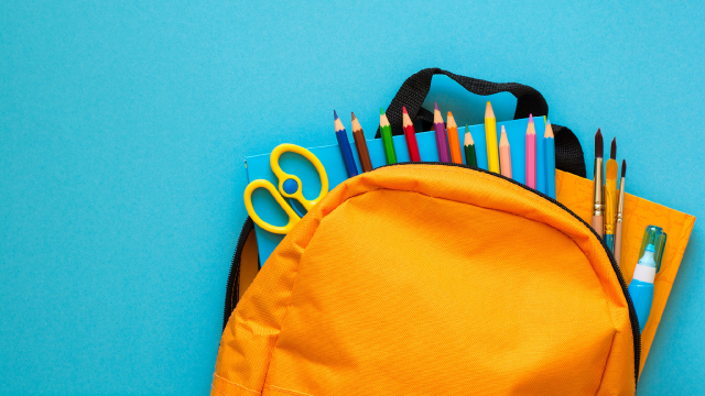 An orange backpack filled with school supplies like colored pencils and scissors on a blue background.