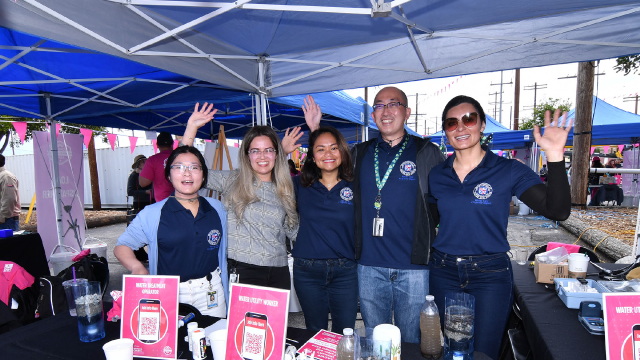 A team of LADWP staff waving and smiling behind their table at a festival booth.