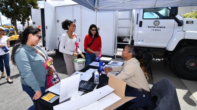 Three women talk to an LADWP staffmember who sits at an event table. An LADWP trailer is in the background. 