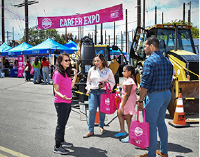 Woman standing on the street talking to a man, a woman and child walking past her. Street banner sign behind her says Career Expo.