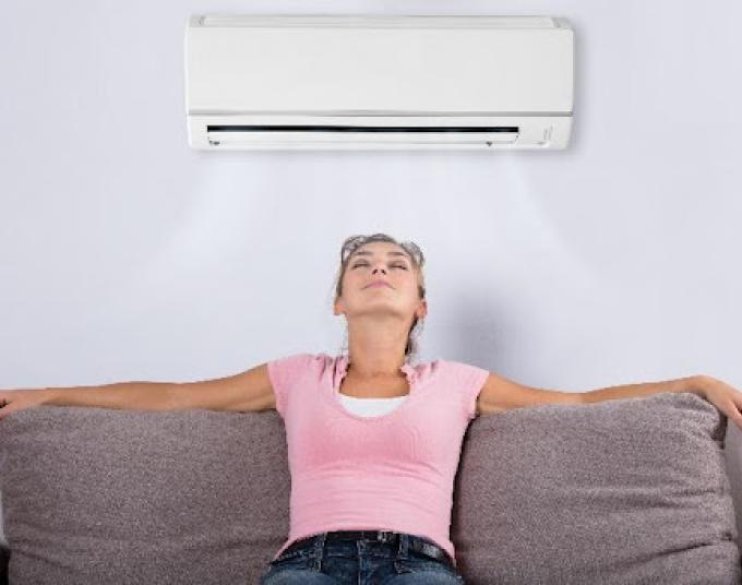 Woman with arms spread across a couch with head leaning back feeling the air conditioner on her face.