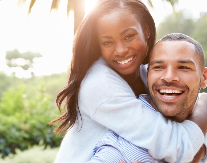 Photo of women hugging man from the back, both smiling looking in to camara.