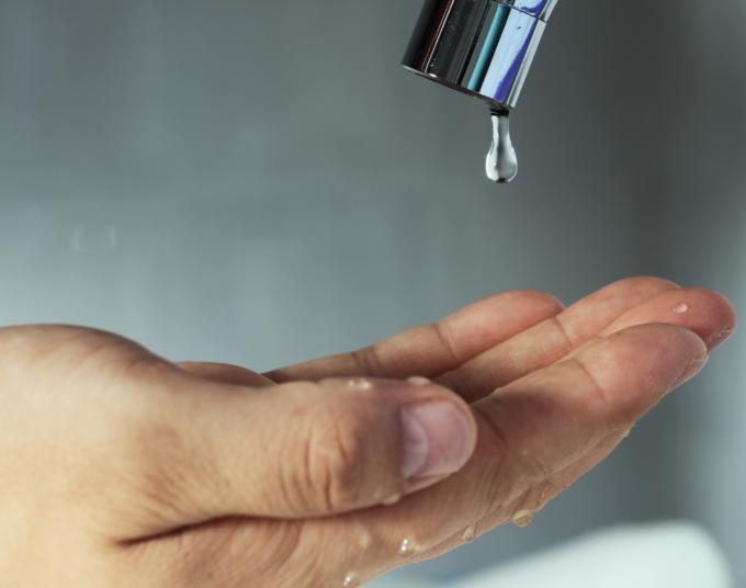 A person reaches out the palm of their hand to catch a drop of water about to fall from a faucet.