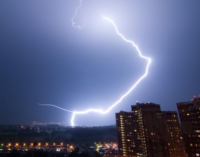 A bolt of lightning strikes a city skyline in the distance.