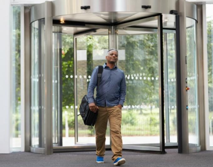 A man walks into a building through a revolving glass door.