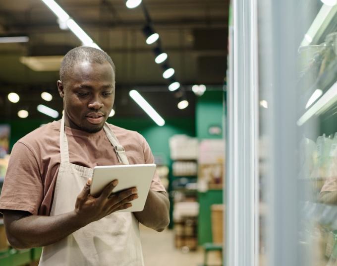 A worker holds a tablet while examining refrigeration at his small business.
