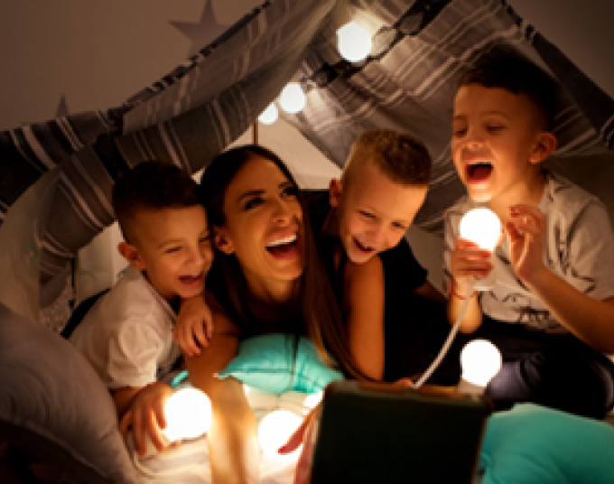 A mother and her three children play in a blanket fort illuminated with LED bulbs.