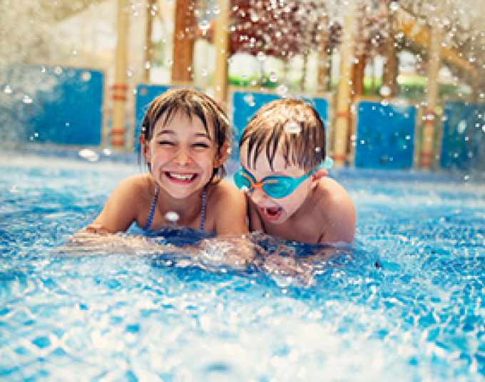 Two smiling children in a pool with water splashing around them.
