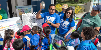 An LADWP water treatment booth. Two LADWP employees talking to seven kids and an adult outdoors.