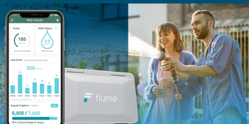 A smartphone showing the Flume mobile app’s display dashboard is beside the Flume smart home water monitoring device. To the right is a smiling woman and a man holding a hose that is spraying water in front of them. The woman has short blonde hair and bangs and is wearing a baby blue cardigan and a pink dress. The man has short brown hair, a trimmed beard and mustache and is wearing a blue jean button-up and checkered pants.